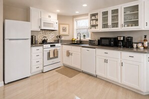 A modern kitchen with white cabinetry, a built-in oven, a microwave, a coffee maker, and a toaster. - Beach House 85-Just One House from the Sand! (Ventura)