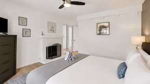 A bedroom with a bed, a fireplace, a ceiling fan, and a television.