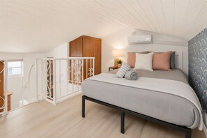 Quarto com cama, mesa de cabeceira, ar condicionado e janela.