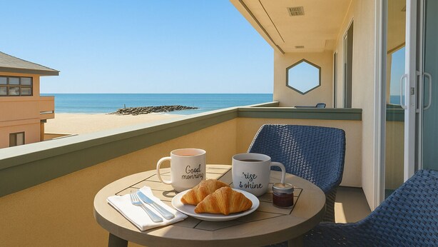 A balcony with a table set for breakfast, overlooking a beach.