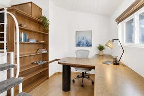 A modern office space with a wooden desk, a bookshelf, a chair, a desk lamp, and a window.