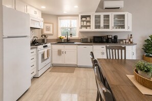 A modern kitchen with white cabinetry, a stove, a sink, and a dining area with a wooden table and chairs.