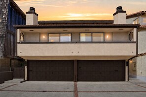 Un edificio residencial de dos pisos con garaje, balcón y vistas al atardecer.