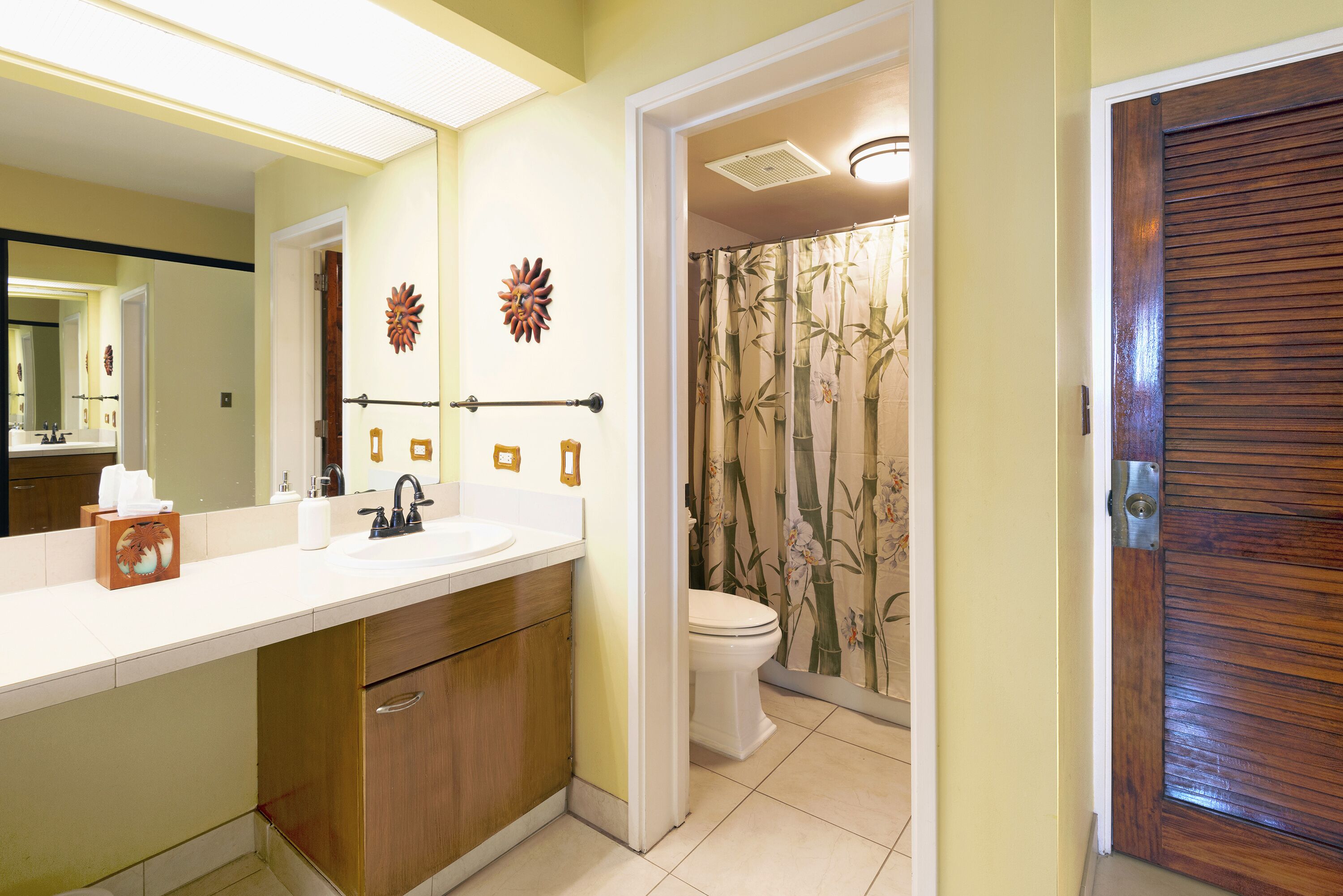 Un baño con lavamanos blanco, armarios de madera, inodoro y ducha con revestimiento de bambú.