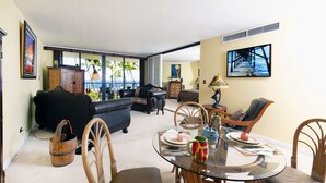 Ein geräumiges Wohnzimmer mit einem Glastisch, bequemen Sitzmöglichkeiten und Meerblick durch große Fenster.