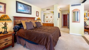 Ein Schlafzimmer mit einem großen Bett, einem Nachttisch, einer Kommode und einem durchgehenden Türrahmen sichtbaren Badezimmer.
