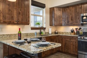 A kitchen with granite countertops, wooden cabinets, a stainless steel oven, and a window with a view.