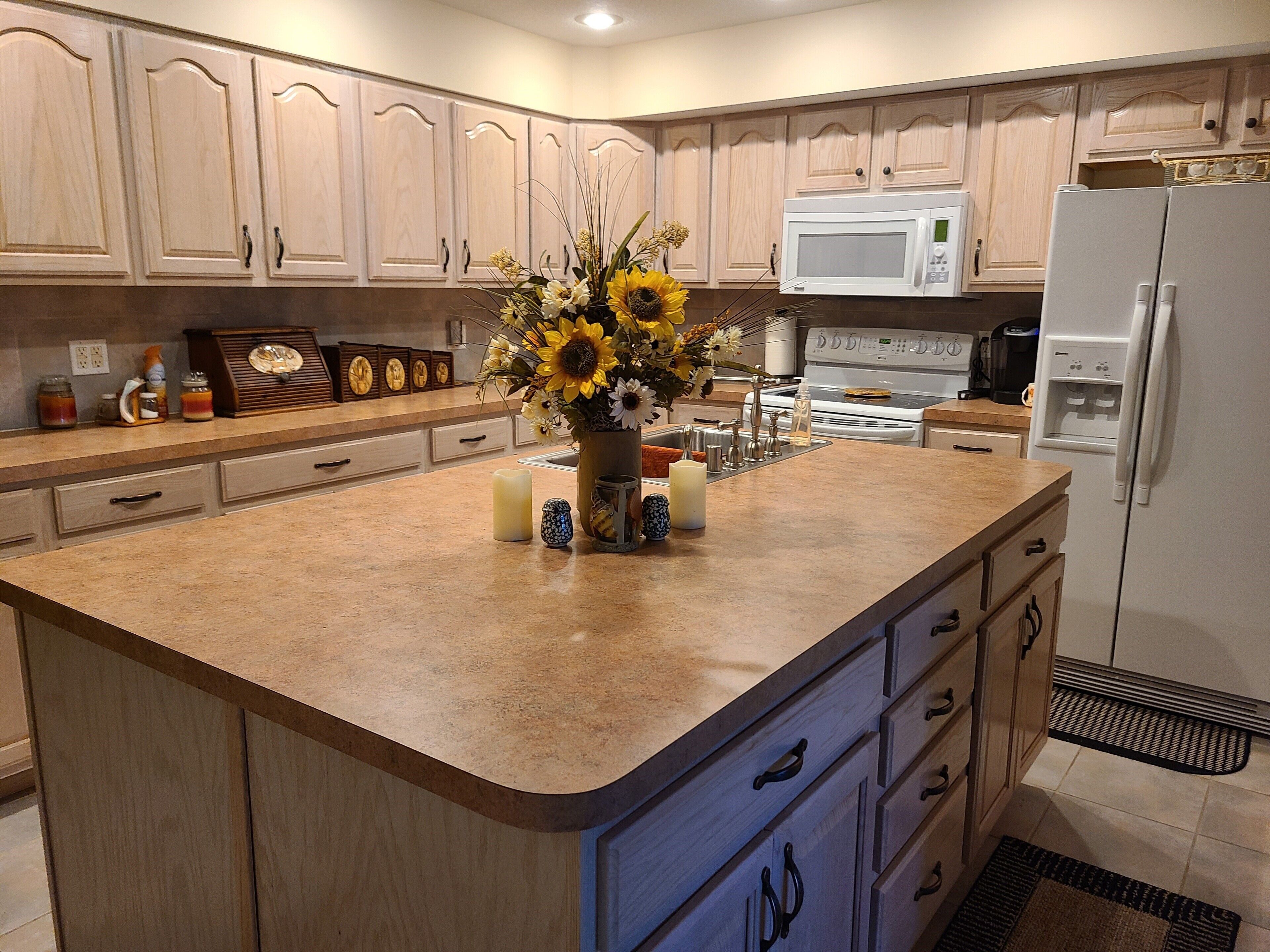 A kitchen with wooden cabinets, a microwave, a refrigerator, and a central island with a vase of flowers.