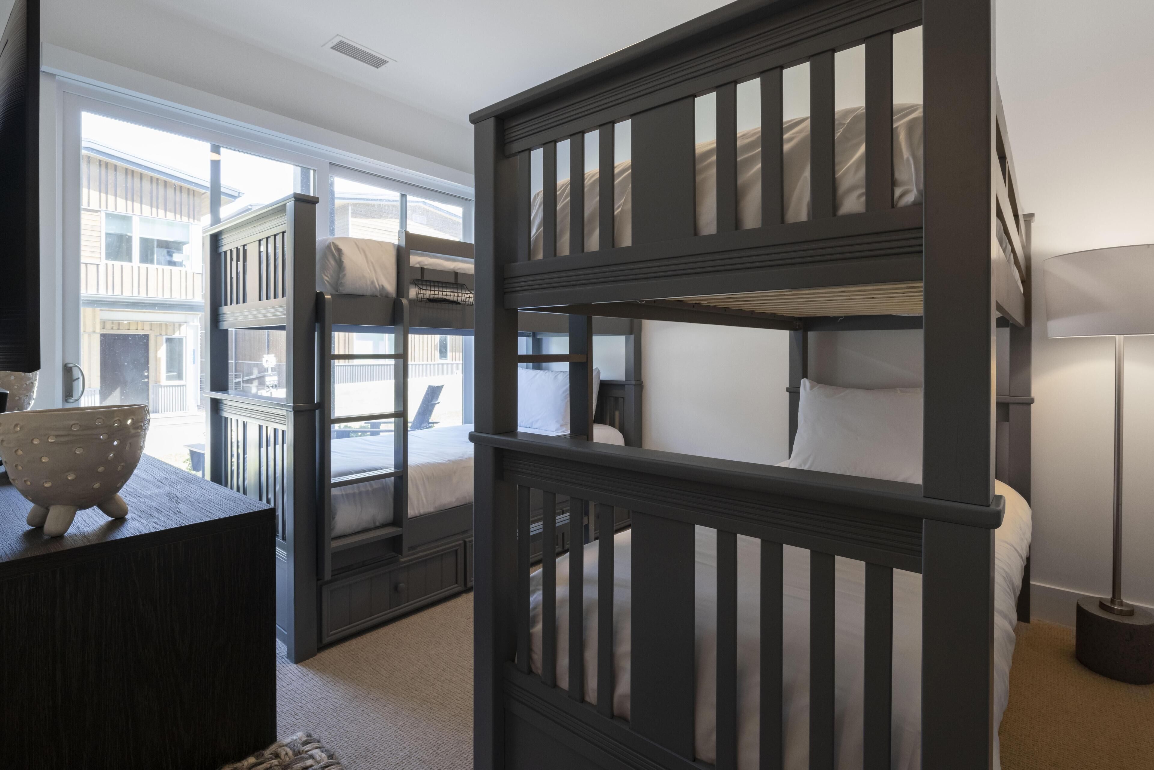 A room with a bunk bed, a desk with a bowl, and a lamp.