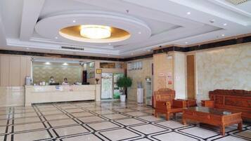 A hotel lobby with a reception desk, seating area, and a large chandelier.
