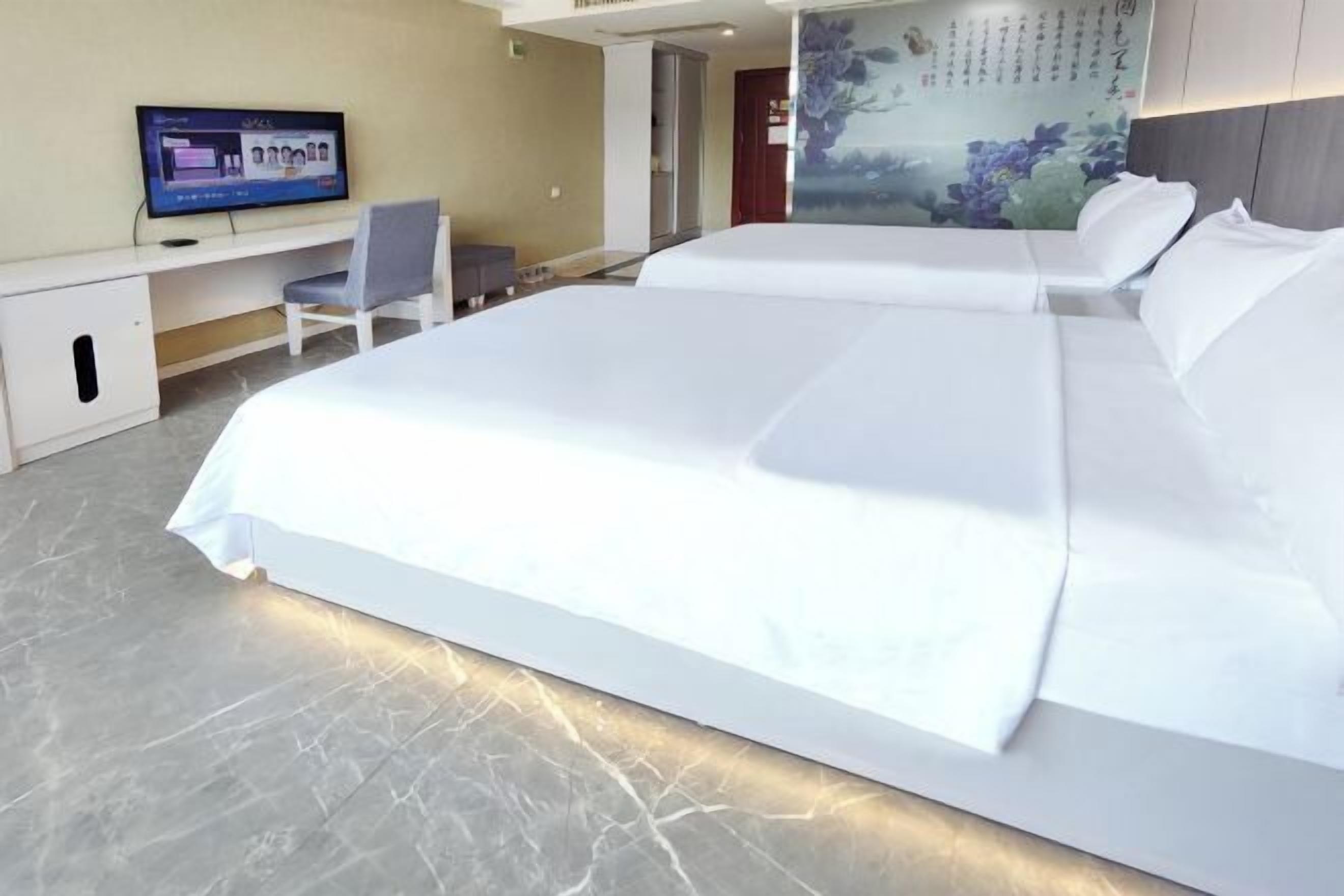 Ein Hotelzimmer mit einem großen Bett, einem Schreibtisch mit Stuhl, einem Fernseher und einer Wand mit einer Blumenmalerei.