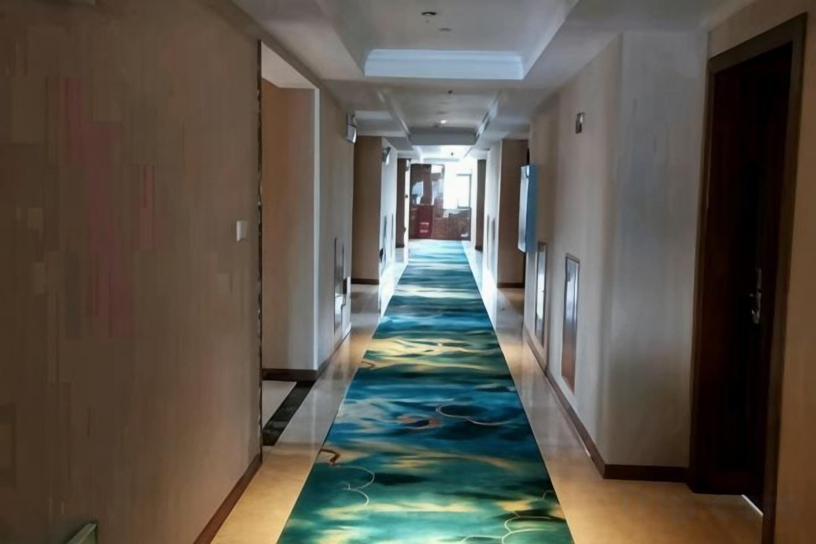 Ein Hotelgang mit einem gemusterten Teppich, Türen an beiden Seiten und einer langen Diele, die zu einem Zimmer führt.