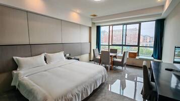 A hotel room with a large bed, a desk, and a view of buildings through the window.