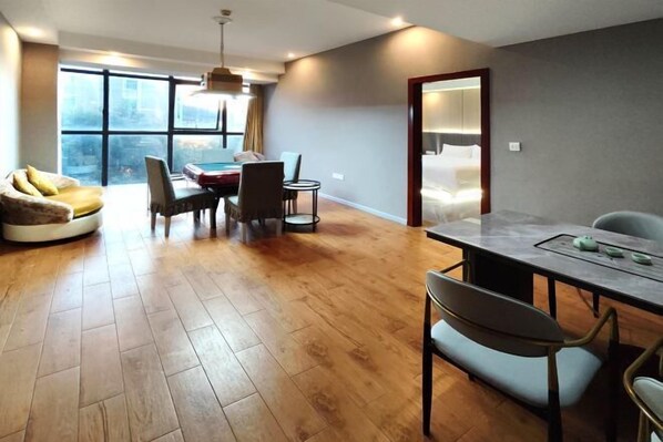 Una habitación de hotel moderna con suelo de madera, una zona de comedor con mesa y sillas, un sofá y un amplio ventanal con vistas a la ciudad.