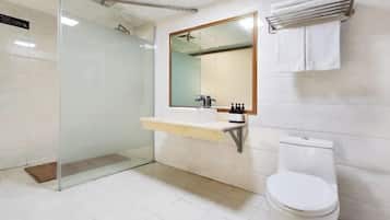 Et moderne badeværelse med et brusekabine i glas, et hvidt toilet, en vask med et spejl over og en håndklædestang på væggen.