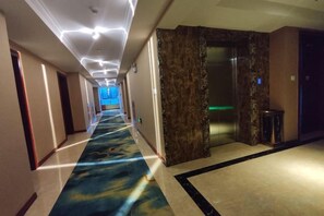 A hotel hallway with a carpeted floor, a marble wall, and a door leading to a room. - Jinglong International Hotel (Yanling)