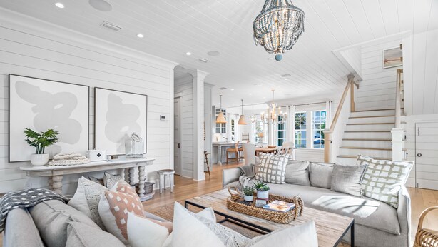 A spacious living room with a large sofa, a coffee table, and a chandelier. There is a staircase leading to another level, and a dining area in the background. - Palm Filled Paradise at Petite Palm / Golf Cart / 3 Min Walk to Beach / Community Pool / 4 Bikes (Santa Rosa Beach)