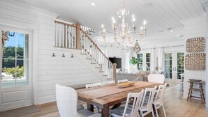 A spacious dining area with a wooden table, white chairs, and a chandelier. - Palm Filled Paradise at Petite Palm / Golf Cart / 3 Min Walk to Beach / Community Pool / 4 Bikes (Santa Rosa Beach)