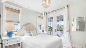 A bedroom with a large bed, two bedside tables with lamps, a mirror, and a view through the glass doors. - Palm Filled Paradise at Petite Palm / Golf Cart / 3 Min Walk to Beach / Community Pool / 4 Bikes (Santa Rosa Beach)