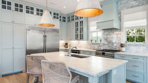 A kitchen with light blue cabinets, a central island with bar stools, stainless steel appliances, and pendant lighting. - Palm Filled Paradise at Petite Palm / Golf Cart / 3 Min Walk to Beach / Community Pool / 4 Bikes (Santa Rosa Beach)