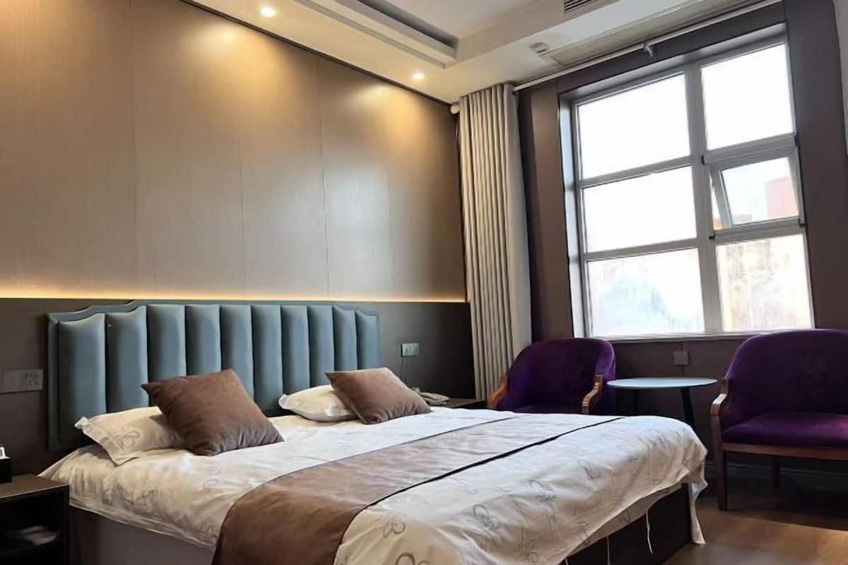 Ein Hotelzimmer mit einem großen Bett, zwei Sesseln, einem kleinen Tisch und einem Fenster mit Vorhängen.