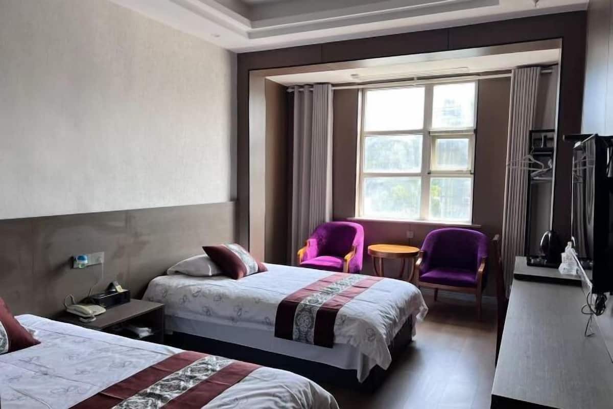 Ein Hotelzimmer mit zwei Betten, einem Schreibtisch, einem Stuhl, einem kleinen Tisch und einem Fenster mit Vorhängen.