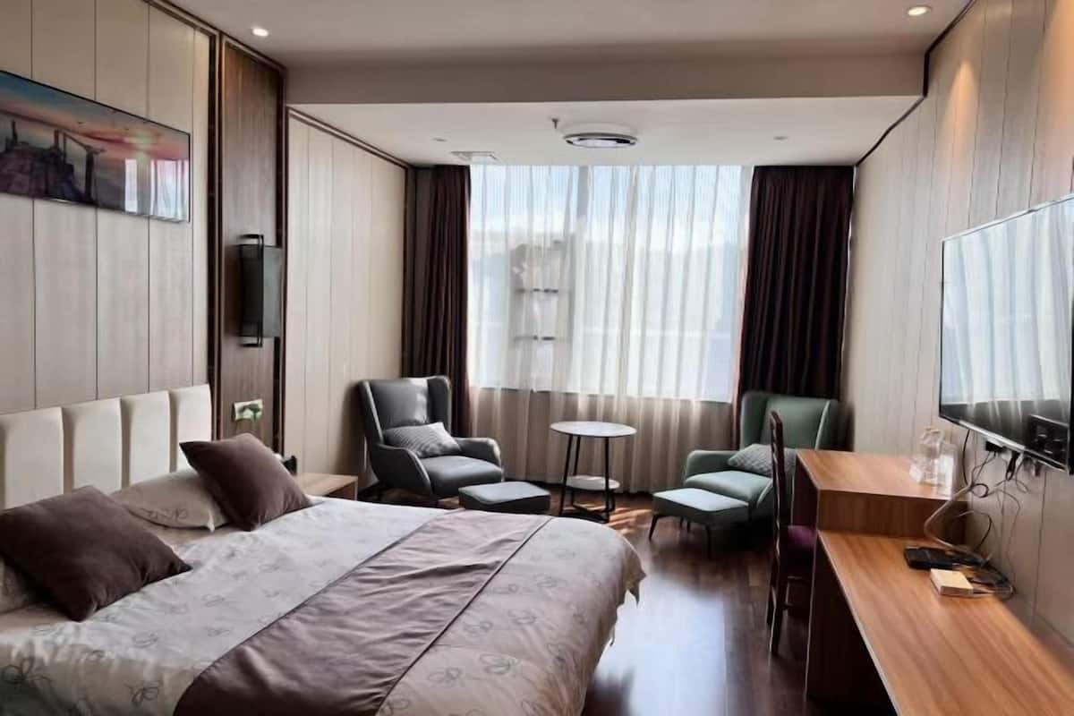 Ein Hotelzimmer mit einem Bett, zwei Sesseln, einem Schreibtisch, einem Fernseher und einem Bild an der Wand.