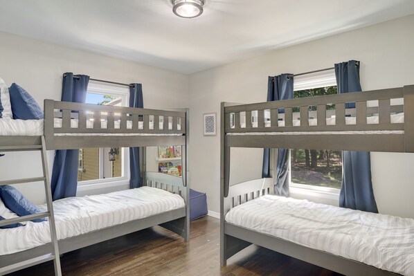 Una habitación con dos literas, una ventana con cortinas, una estantería y un pequeño reposapiés azul.