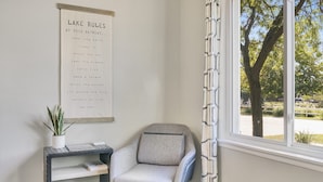 A corner of a room with a chair, a small table with a plant, and a window with a view of trees and a parking lot. - ❤ 5 Min Walk to Beach Fast Wi-Fi Arcade Games ❤ (Muskegon)