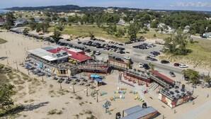 An aerial view of a beachside resort with a large parking lot, beach chairs, umbrellas, and a building with a red roof. - ❤ 5 Min Walk to Beach Fast Wi-Fi Arcade Games ❤ (Muskegon)