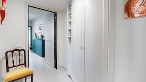 Un couloir avec une chaise en bois, une armoire blanche et un tableau accroché au mur.