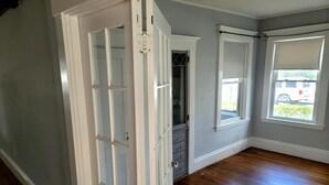 Habitación con suelo de madera, una puerta blanca y ventana con vista a un vehículo fuera.