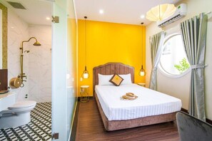 A hotel room with a bed, bedside lamps, a window with curtains, a bathroom with a toilet and shower, and a patterned floor.