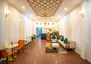 A spacious hotel lobby with a central seating area, a reception desk, and a chandelier.