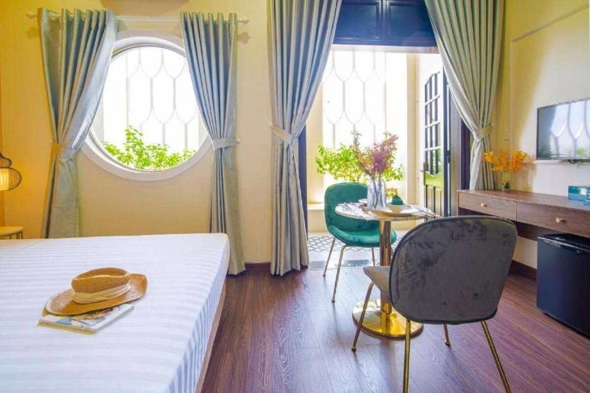 Habitación de hotel con cama, escritorio, silla, mesita y ventana con cortinas.