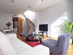 A modern living room with a sofa, armchair, TV, and a staircase leading to another room.