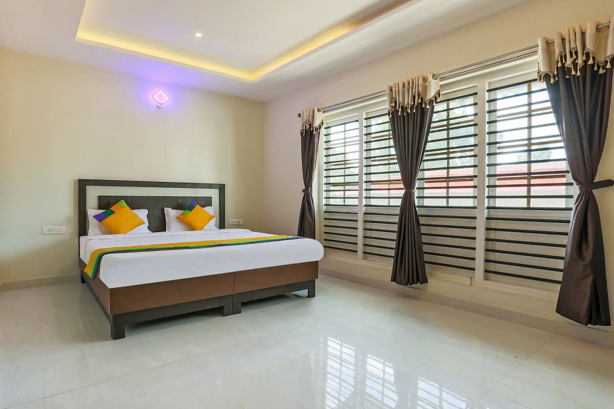 A hotel room with a bed, a window with blinds, and a ceiling light.