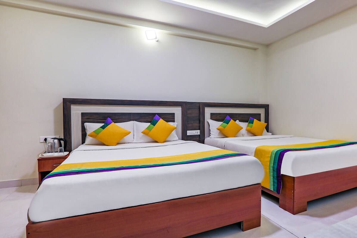 A hotel room with two beds, each with a white bedspread and colorful pillows.