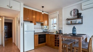 Eine moderne Küche mit Holzausstattung, einem weißen Kühlschrank, einem Einbauofen und einem Essbereich mit Tisch und Barhocker.