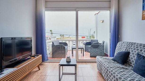 Ein Wohnzimmer mit Fernseher, einer Couch und einem Balkon mit Gartenmöbeln.