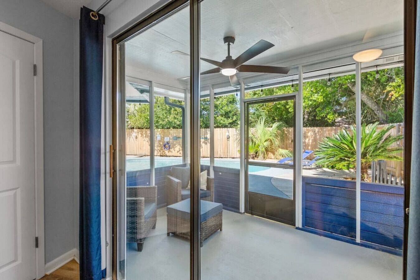 A covered patio with a ceiling fan, outdoor furniture, and a view of a backyard with a pool.
