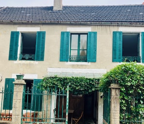 Un bâtiment à deux étages avec des volets verts, un auvent blanc et un pilier en pierre.