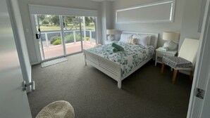 A bedroom with a bed, a chair, a nightstand, a ceiling fan, and a view through a sliding glass door.