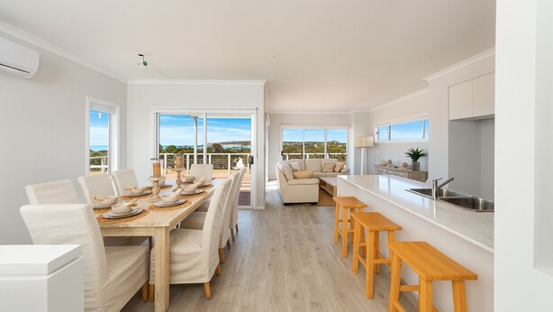 A modern kitchen with a dining area, wooden flooring, and large windows offering a view.