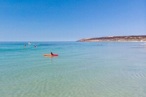A clear beach with calm waters, a sandy shore, and a distant hill.