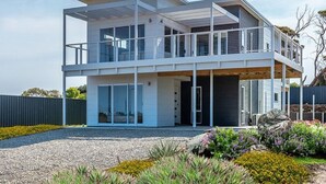 A modern two-story house with a balcony, large windows, and a gravel driveway.