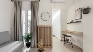 A modern living room with a grey sofa, a coffee table, a potted plant, and a wooden partition. There is a round mirror on the wall and a small table with stools. - Dreamy 1BR Apartment in Kolonaki (Athens)
