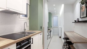 A narrow kitchen with white cabinets, a black countertop, and a wooden bench. - Dreamy 1BR Apartment in Kolonaki (Athens)