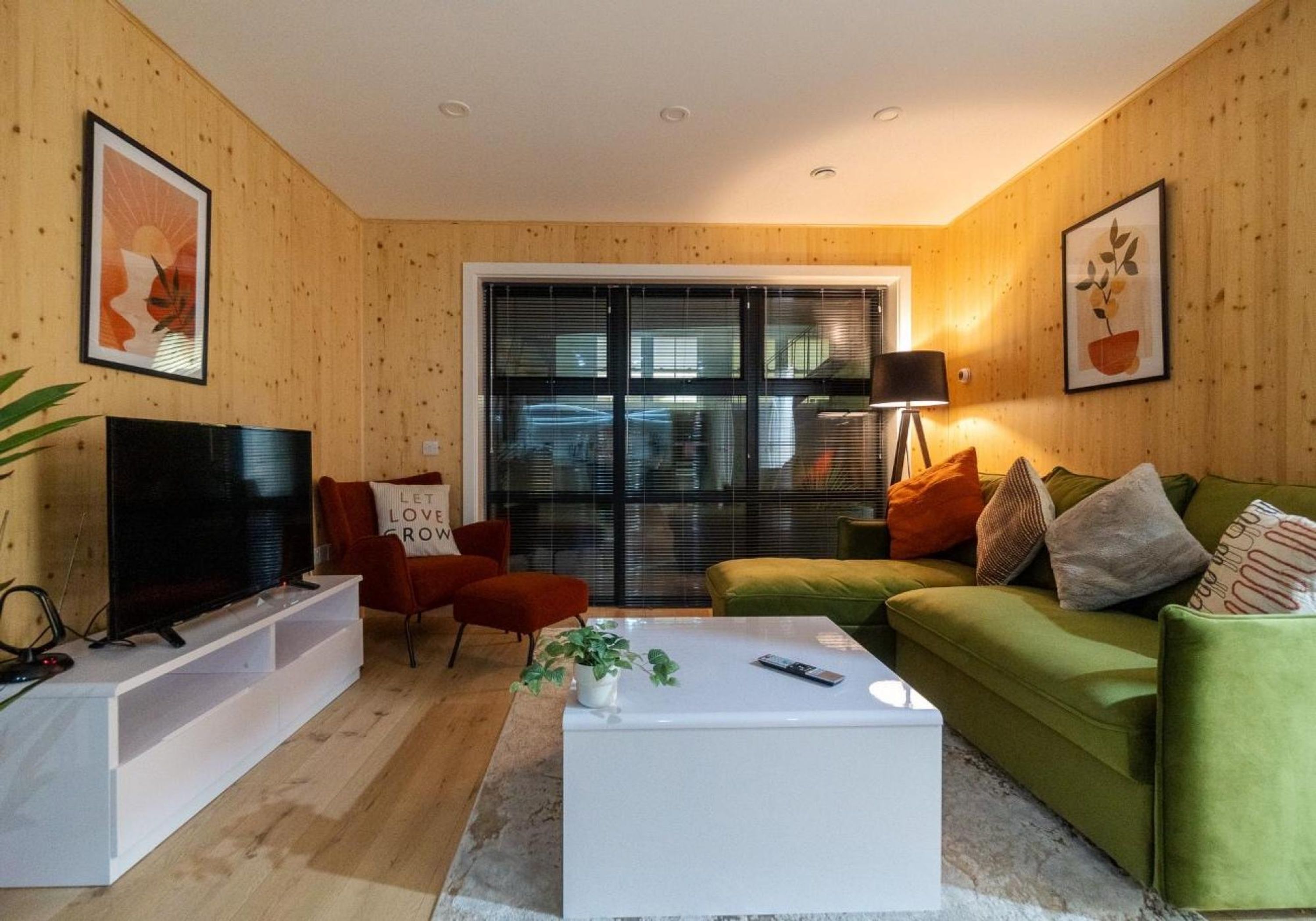 Una sala de estar moderna con un televisor de pantalla plana, un sofá verde, una mesa de centro blanca y un sillón rojo.