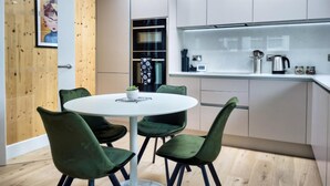 A modern kitchen with white cabinets, a round dining table, and green chairs. - Green Mews 3 By My Getaways (Hove)